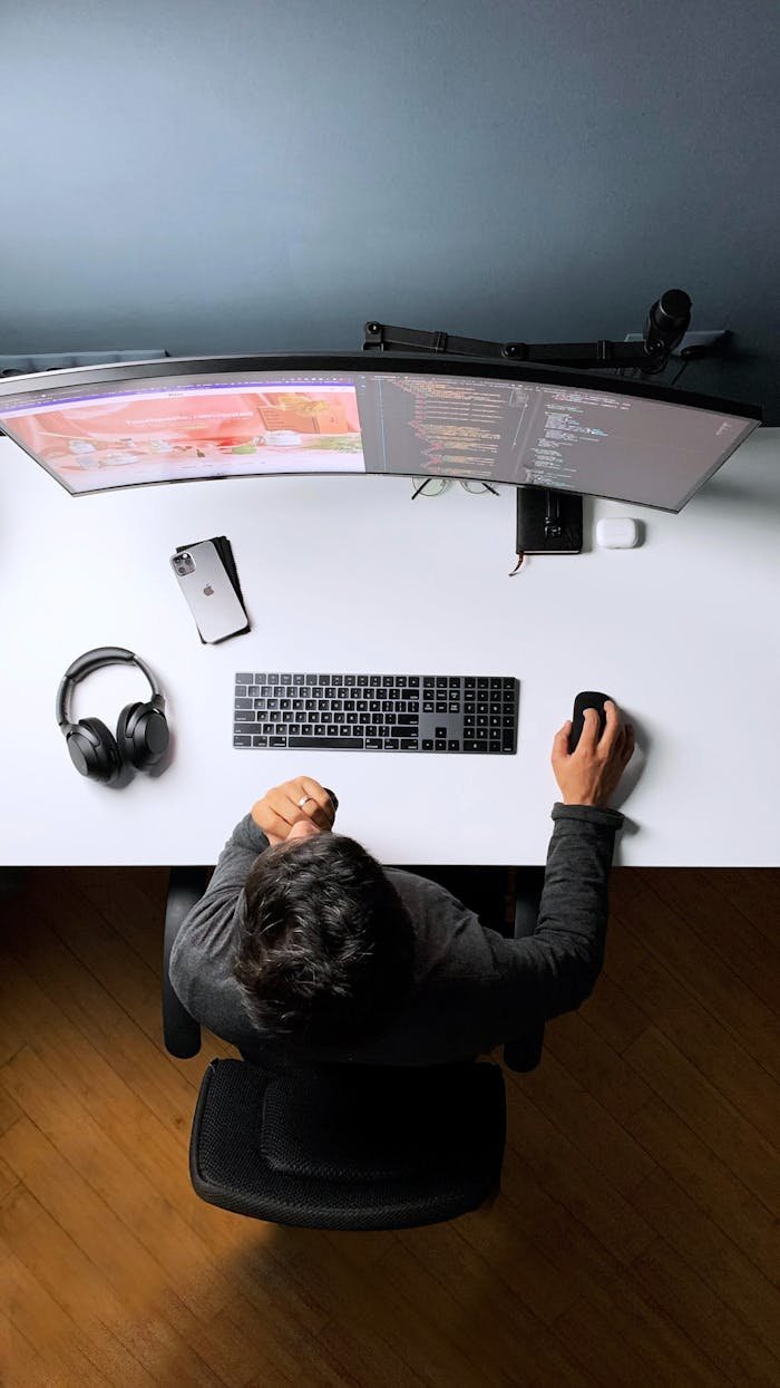 Top view of a person working at a computer desk with dual monitors, headphones, and smartphone.