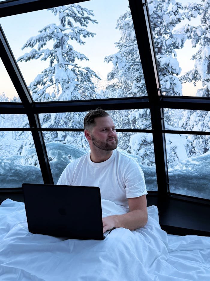 services-02 A man using a laptop inside a glass dome surrounded by snowy trees in Finland.