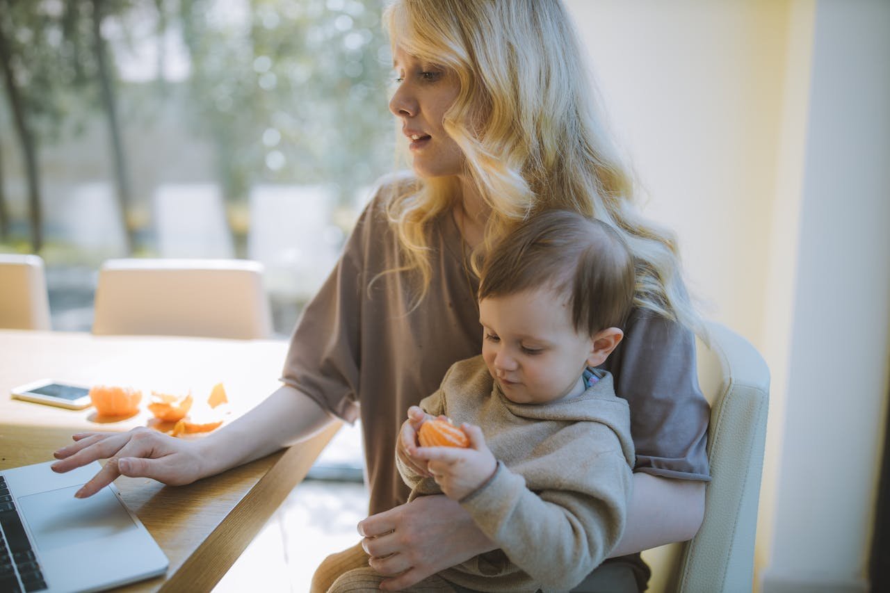 Mother working on laptop while holding her child, embodying work-life balance.