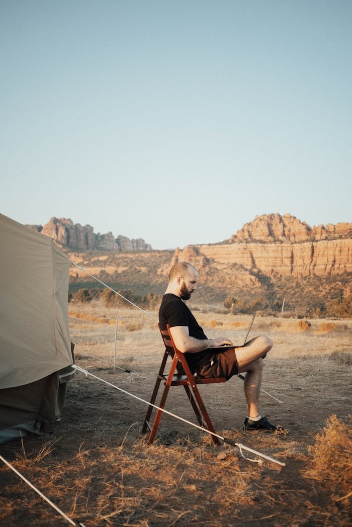 services-03 Man working on a laptop at a desert campsite, showcasing remote work lifestyle.