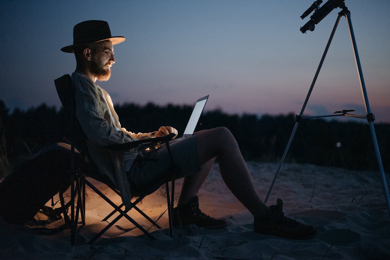 gallery-5 A man sitting on a beach with a laptop and telescope, enjoying the sunset.