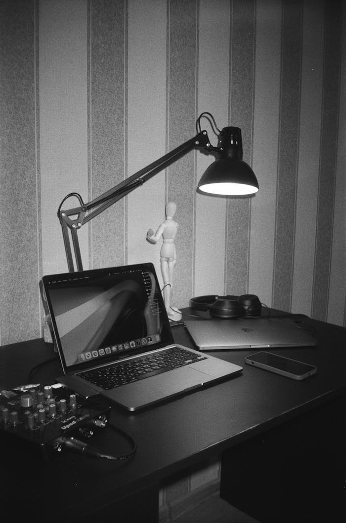 gallery-4 Grayscale photo of a modern desk setup with a laptop, lamp, and office accessories.