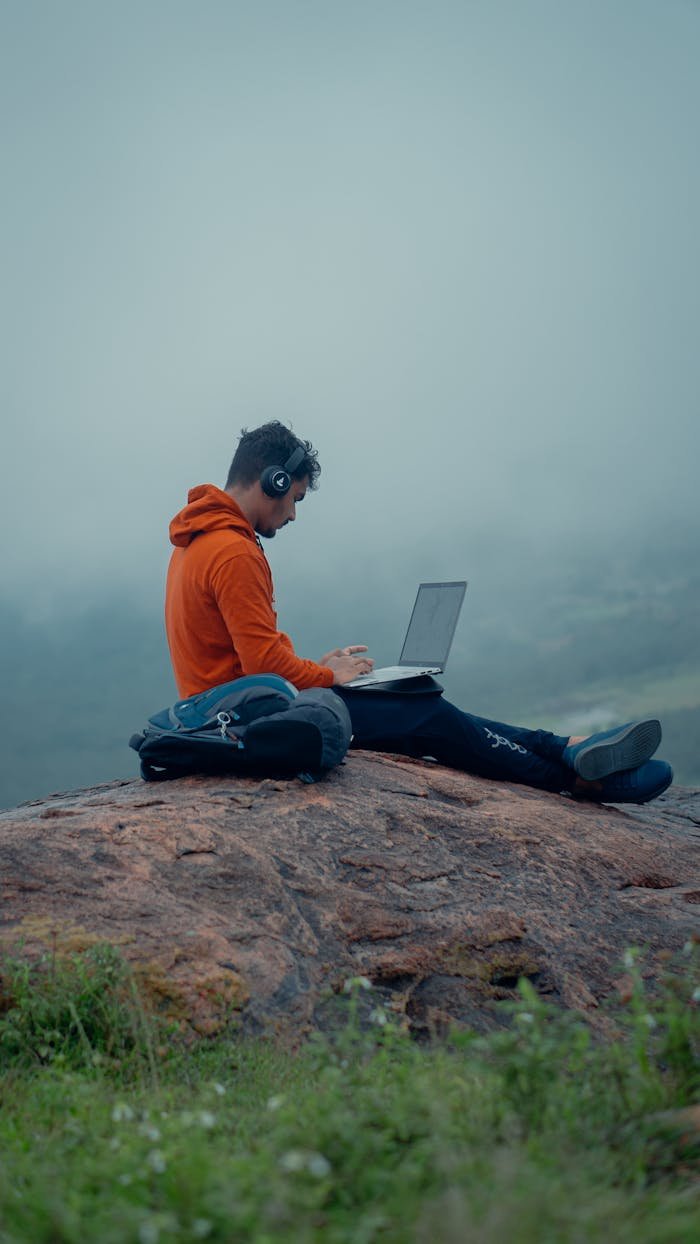 about-01 Man seated on a rock with laptop and headphones, embracing remote work in nature.